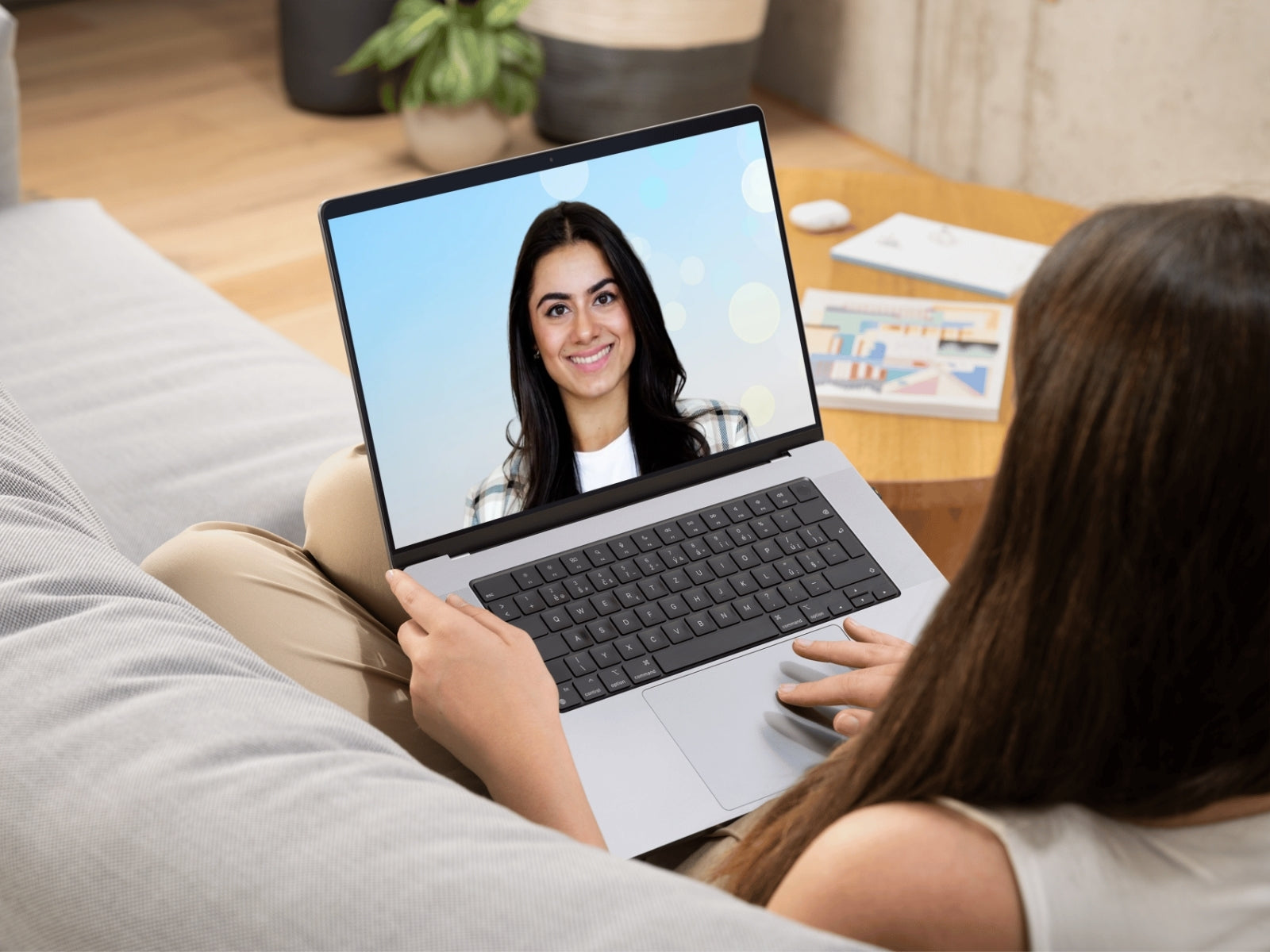 Client using a laptop with a video call on screen, sitting on a couch.