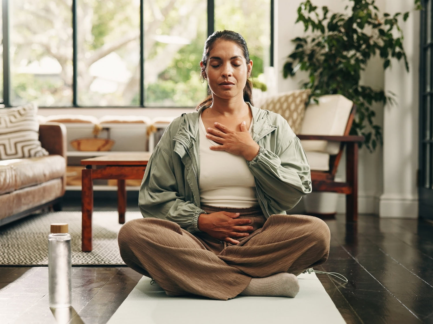 Woman practicing yoga in a living room with a water bottle nearby